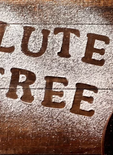 The words gluten-free written in flour with a loaf of gluten-free bread on the side.