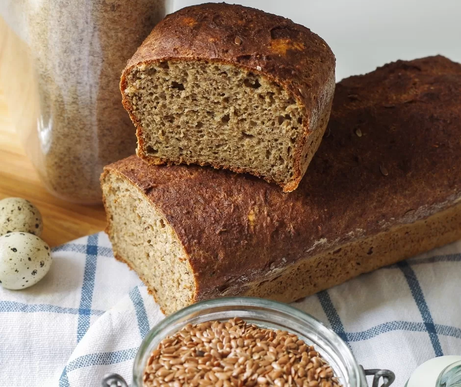 Psyllium flaxseed bread on a cutting board with whole flaxseeds, psyllium husk and milk.