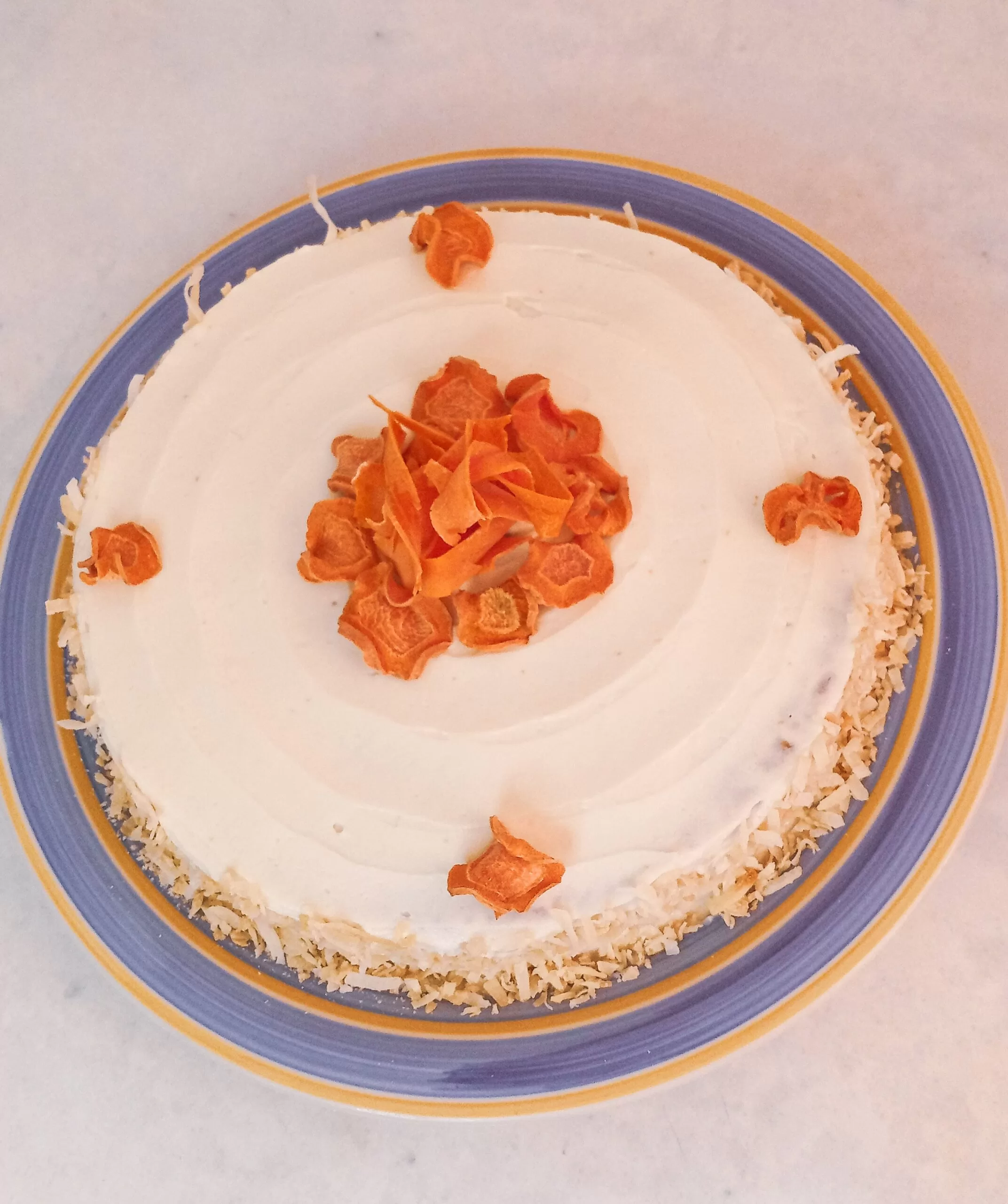 Gluten-free carrot cake decorated with sugar-free cream cheese frosting and dehydrated carrot chips on a plate.