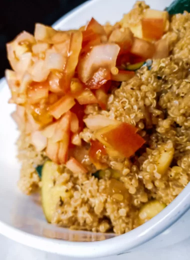 Zesty quinoa zucchini salad in a serving dish topped with fresh tomatoes.