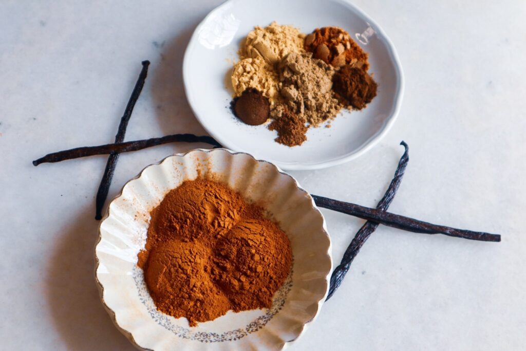 Ingredients for vanilla chai spice in a bowl and a plate along with a vanilla bean.