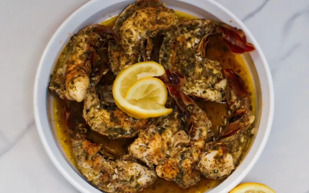 Baked garlic butter lobster tails in a baking dish garnished with lemon slices.