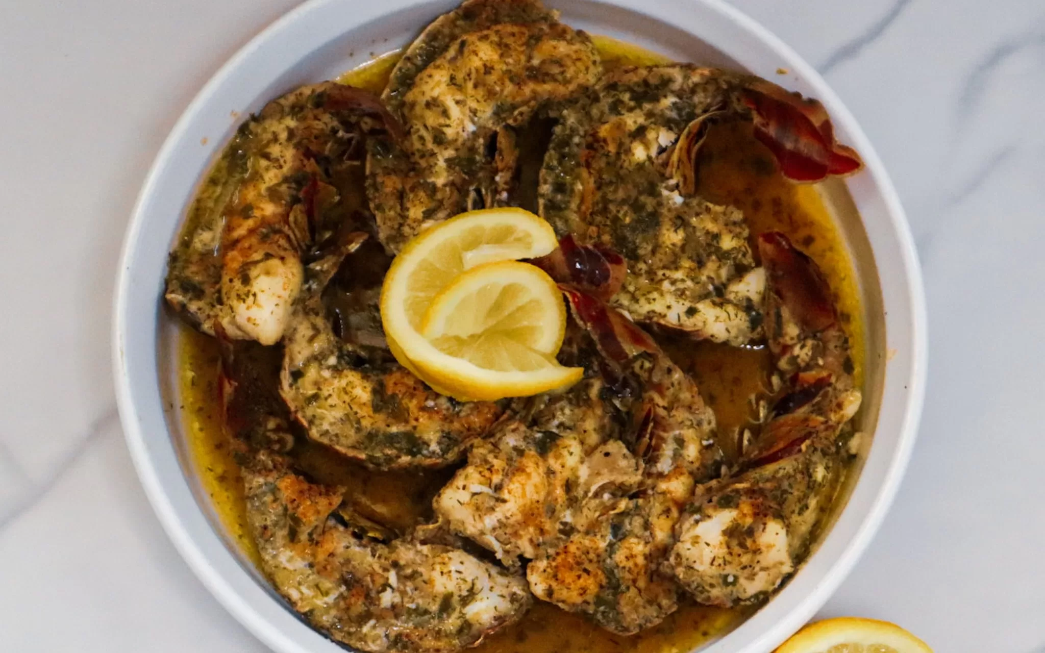 Baked garlic butter lobster tails in a baking dish garnished with lemon slices.