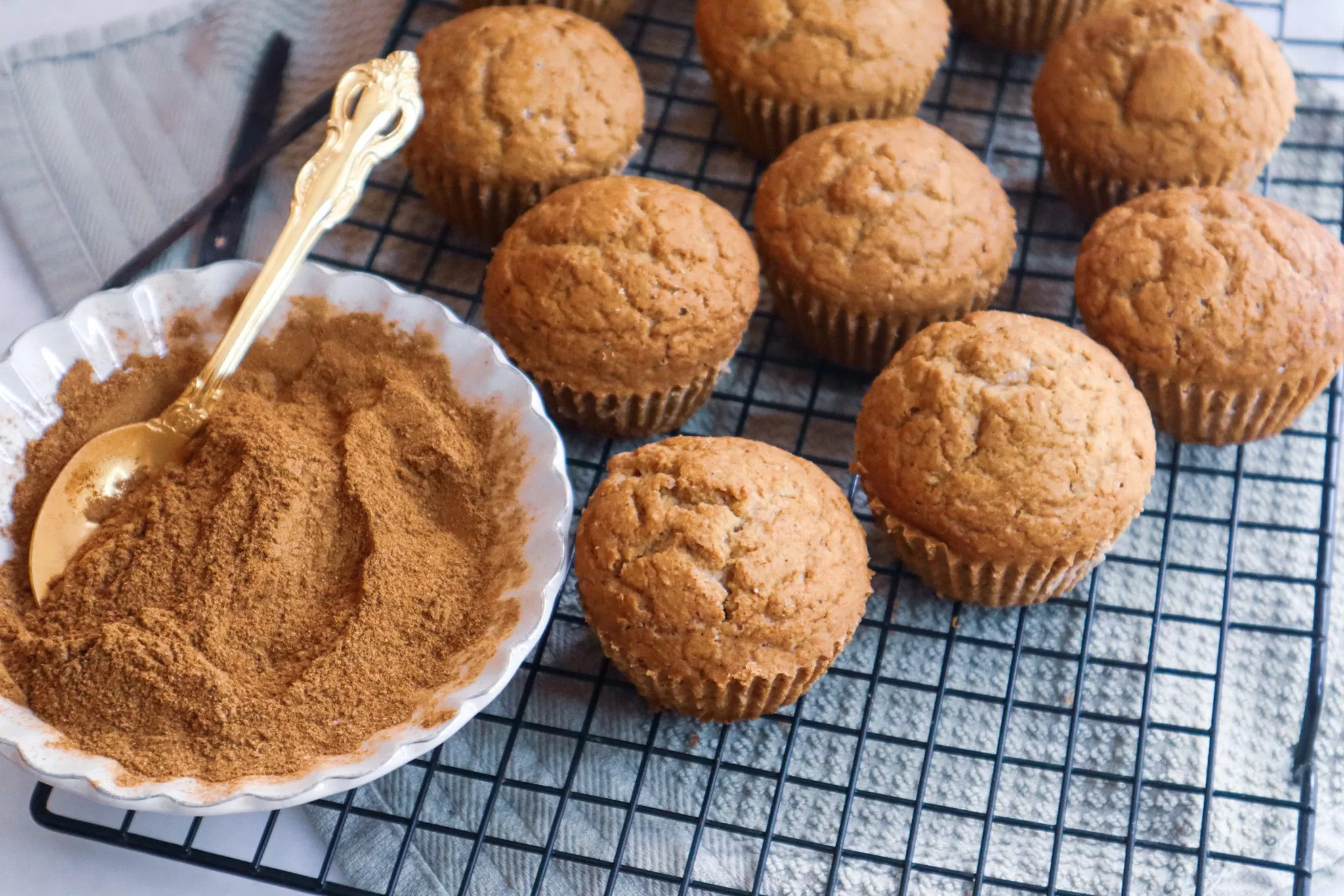 Gluten-free apple butter muffins on a cooling rack with chai spice mix in a small bowl.