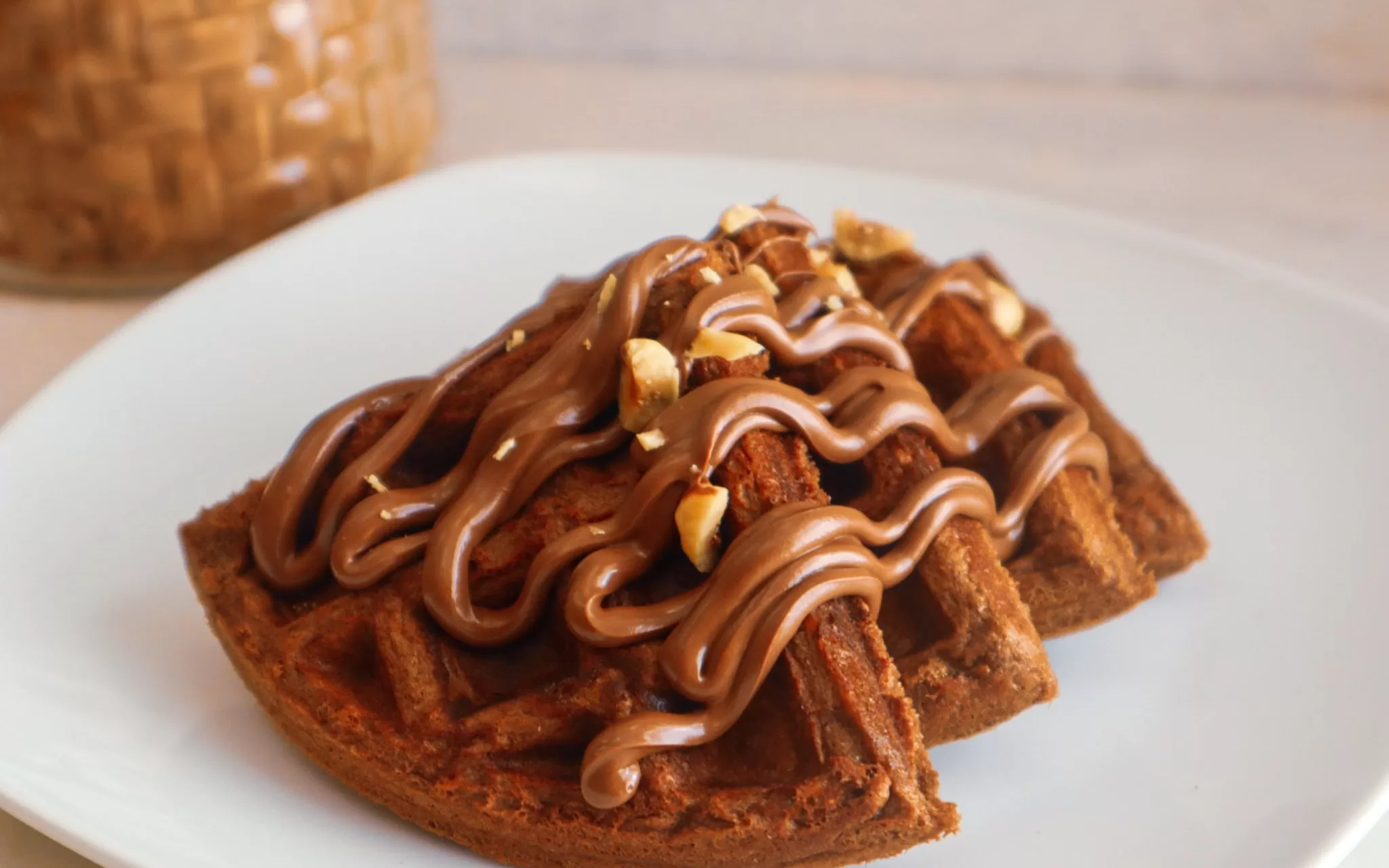 Gluten-free chocolate hazelnut waffles on a plate garnished with sugar-free chocolate hazelnut spread and hazelnuts.