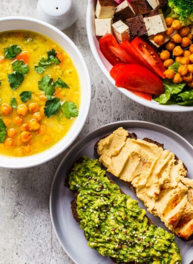 Chocolate smoothie bowl, lentil chickpea soup, tofu Buddha bowl, and toasts arranged on the countertop,