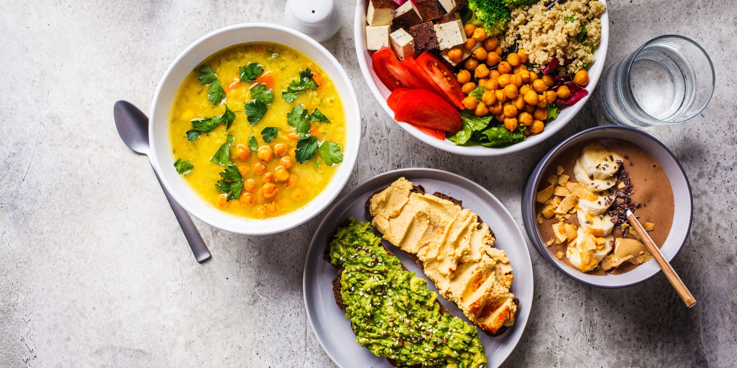 Chocolate smoothie bowl, lentil chickpea soup, tofu Buddha bowl, and toasts arranged on the countertop,