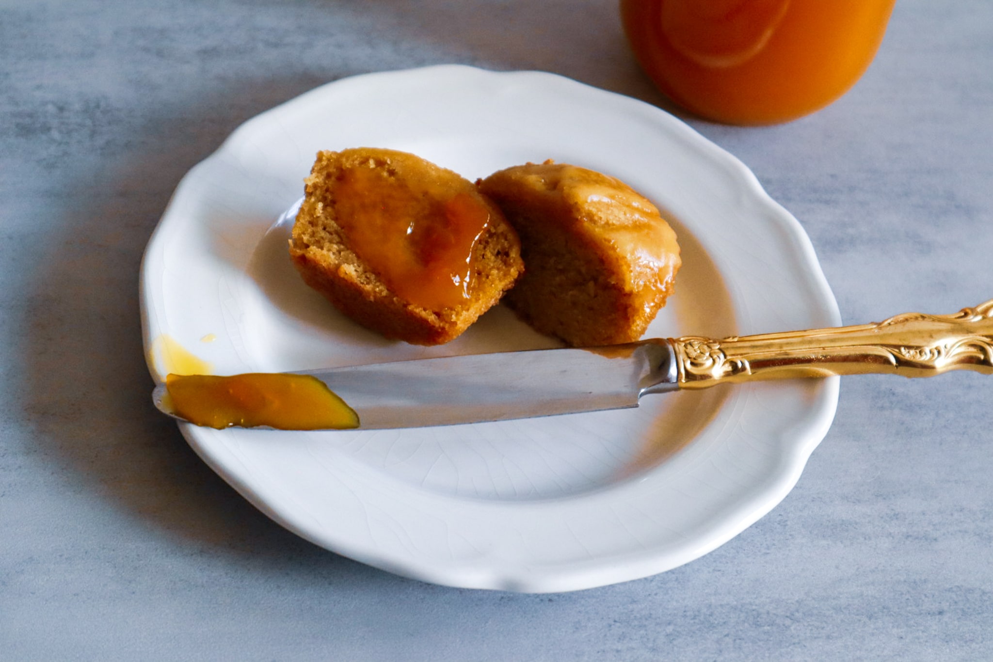 A mango muffin slathered with mango jam on a plate next to a jar of mango jam.