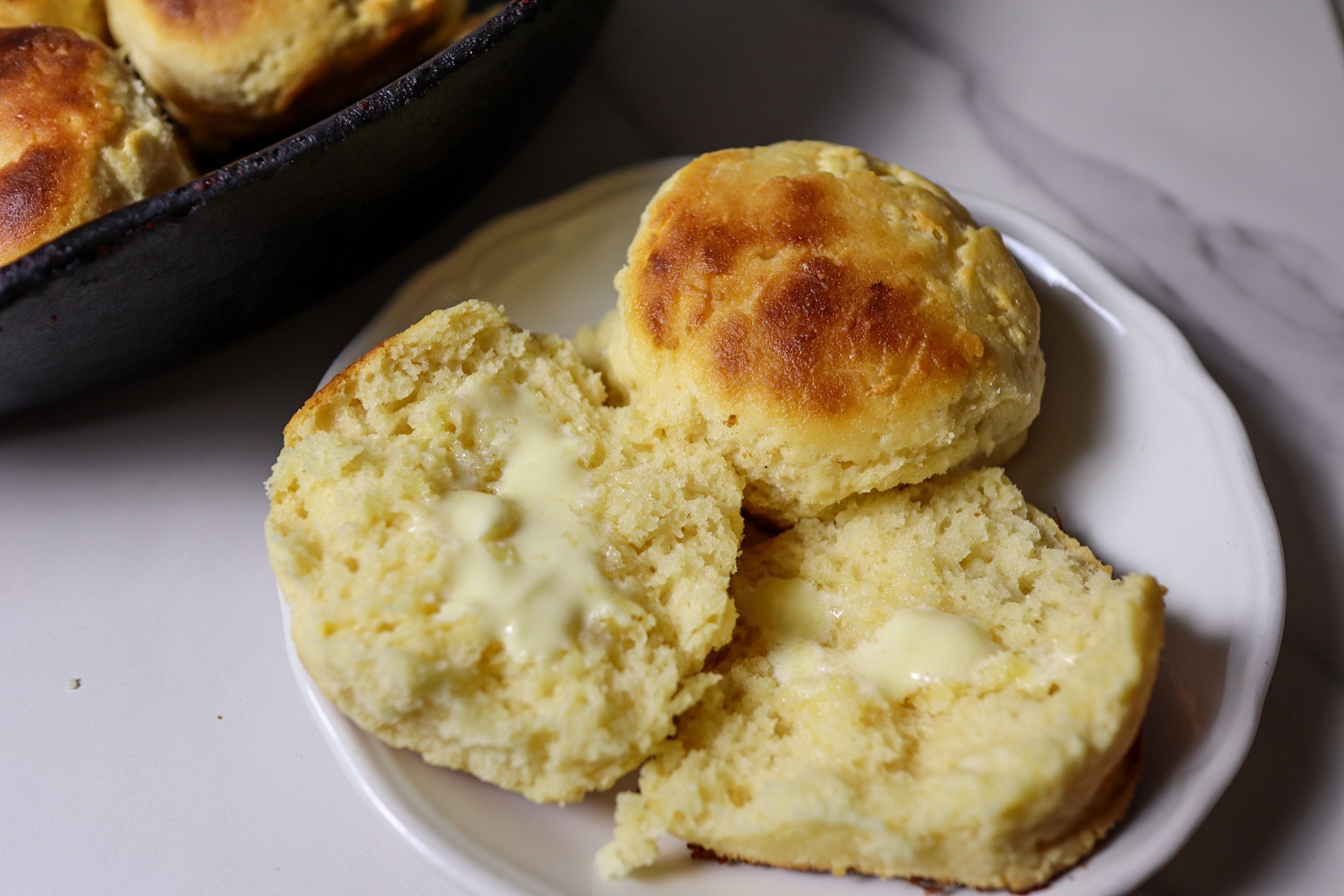 Gluten-free biscuits on a plate smeared with butter.