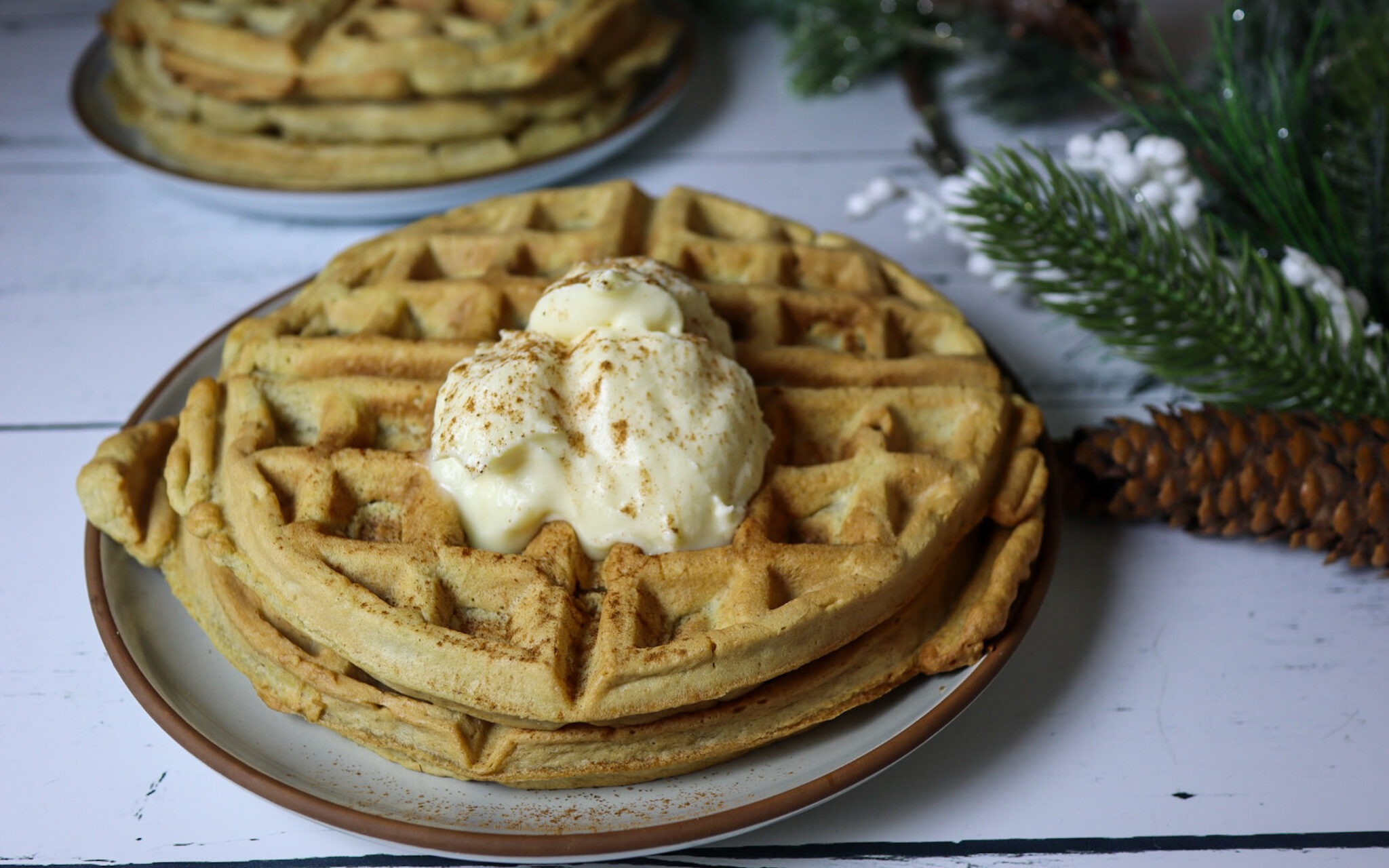 Gluten-free eggnog waffles on a plate topped with cream cheese frosting and sprinkled cinnamon.