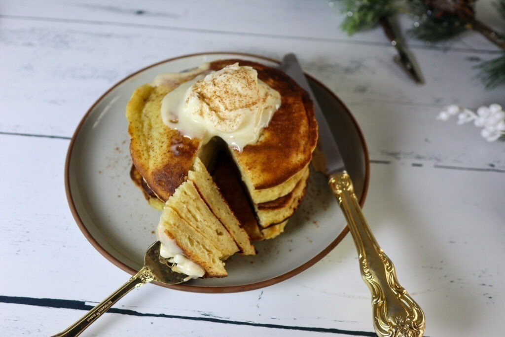 Gluten-free eggnog pancakes on a plate garnished with cream cheese frosting and cinnamon.