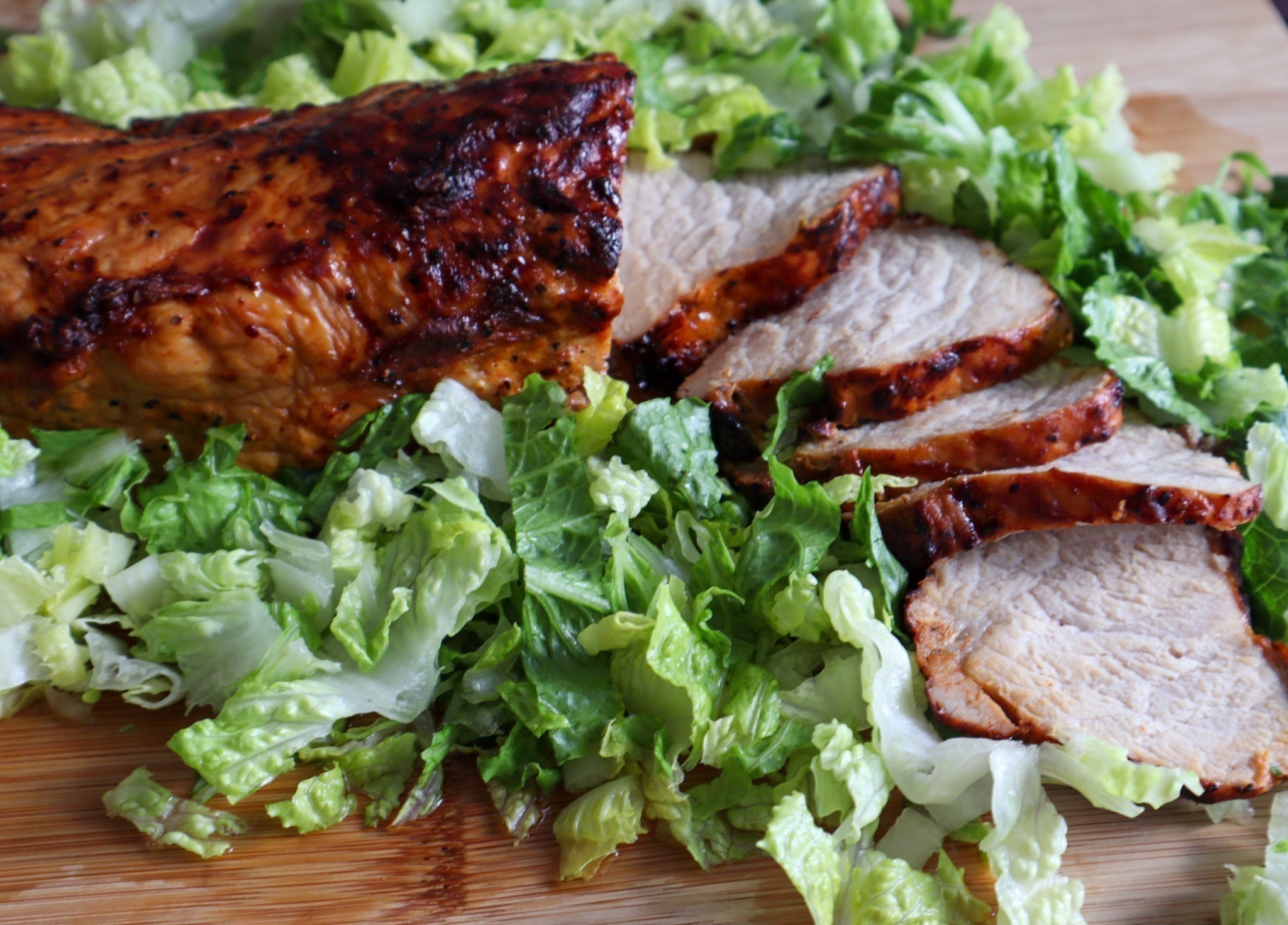 Air fryer BBQ pork tenderloin on a cutting board with fresh romaine lettuce.