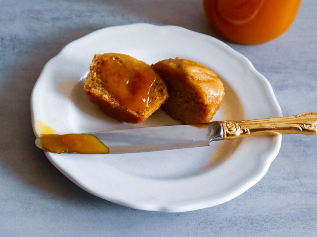 A mango muffin slathered with mango jam on a plate next to a jar of mango jam.
