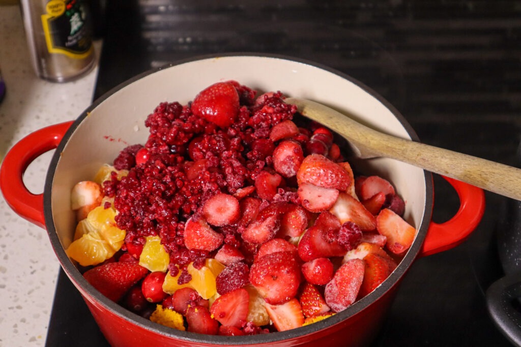 Adding the strawberry cranberry jam ingredients to a Dutch oven.