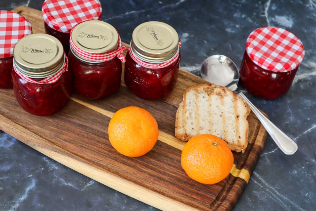 Canned strawberry cranberry jam with fresh oranges and a slice of gluten-free bread.
