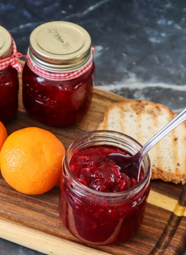 Canned strawberry cranberry jam with fresh oranges and a slice of gluten-free bread.