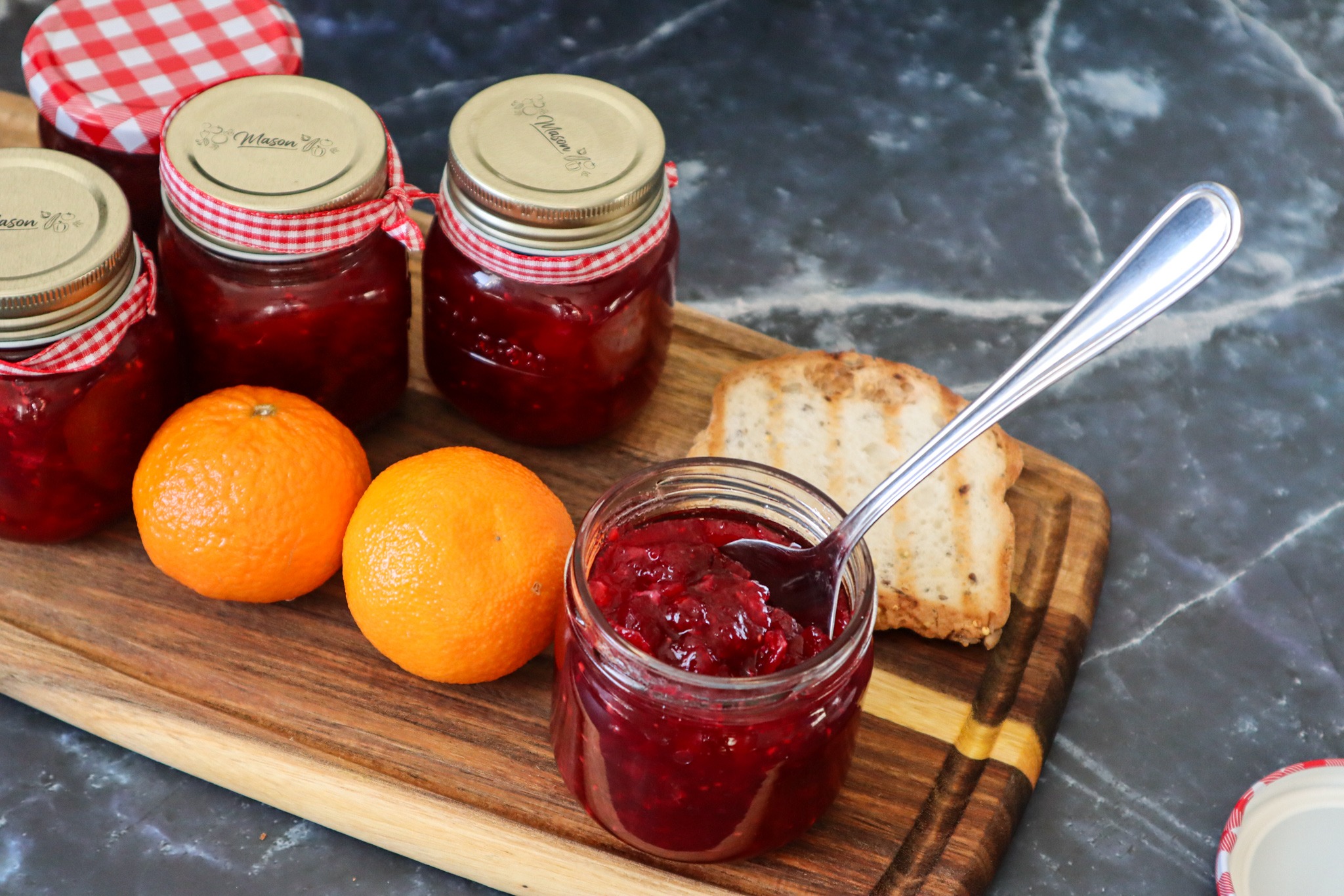 Canned strawberry cranberry jam with fresh oranges and a slice of gluten-free bread.