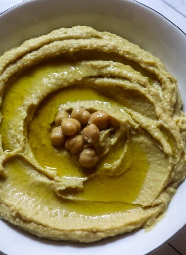 Homemade hummus in a serving bowl, garnished with olive oil and chickpeas.