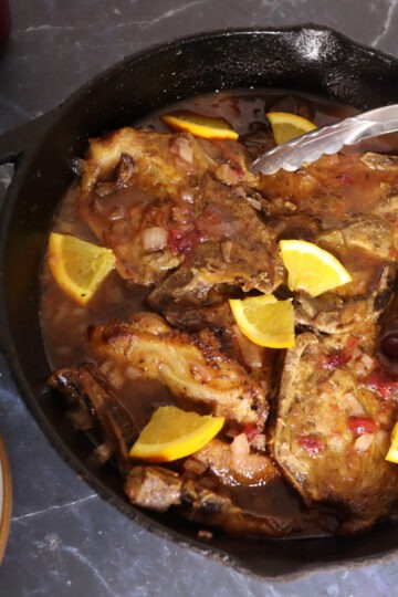 Cranberry pork chops in a skillet with cranberry jam in the background.