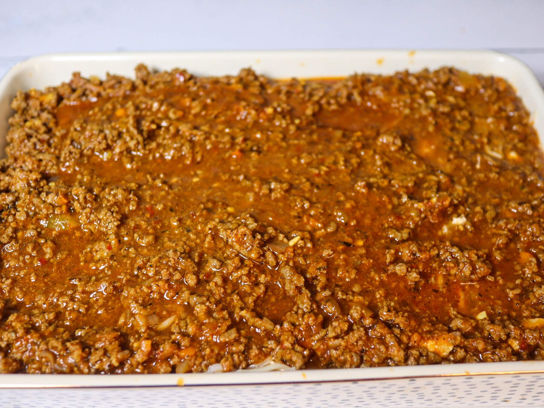 Spreading the meat sauce on top of the cheese layer.
