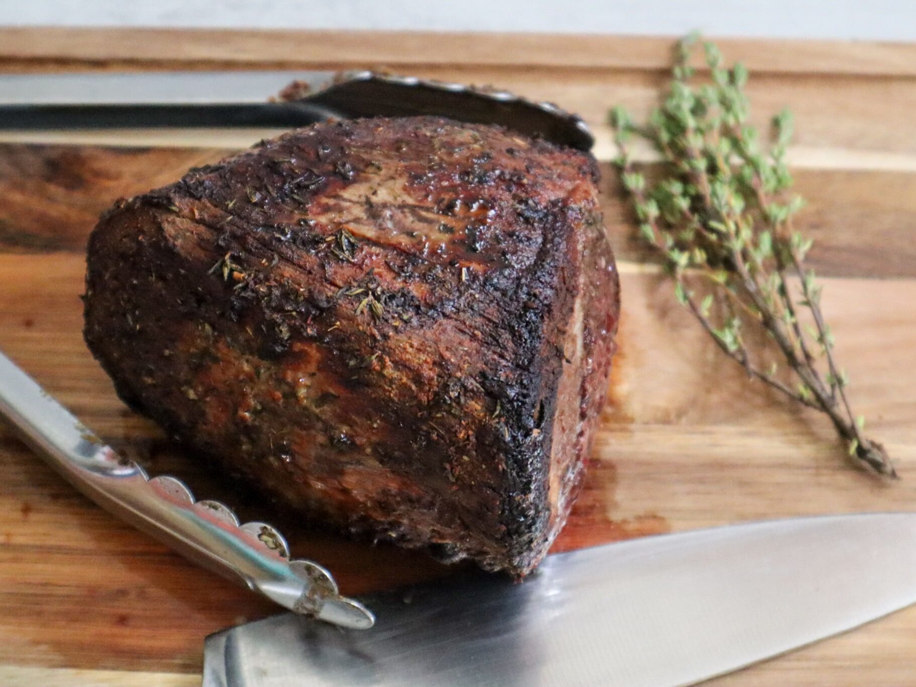 Air fryer roast beef on a cutting board garnished with fresh thyme.