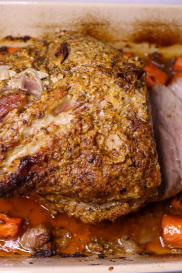 Roasted pork shoulder in a roasting pan with carrots and onions.