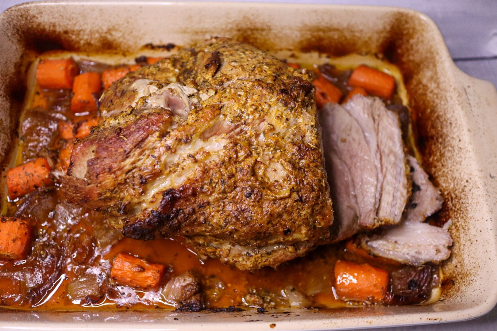 Roasted pork shoulder in a roasting pan with carrots and onions.